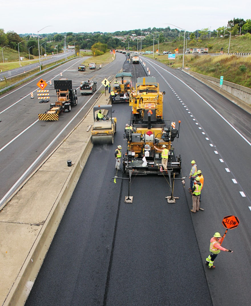 construction crew laying and rolling asphalt on a roadway