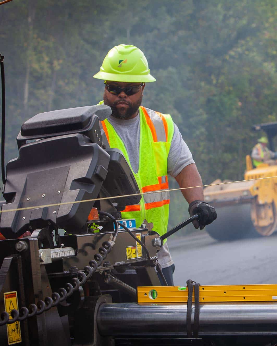 construction worker manning an asphalt paver on job site