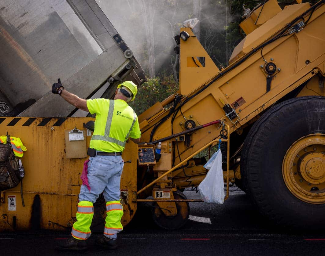 construction worker directing a truck to unload asphalt on job site
